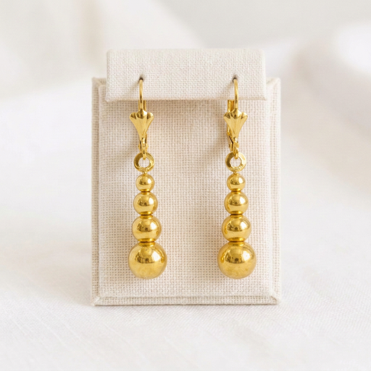 Paire de boucles d’oreilles boules dégradées en plaqué or sur présentoir en lin ivoire