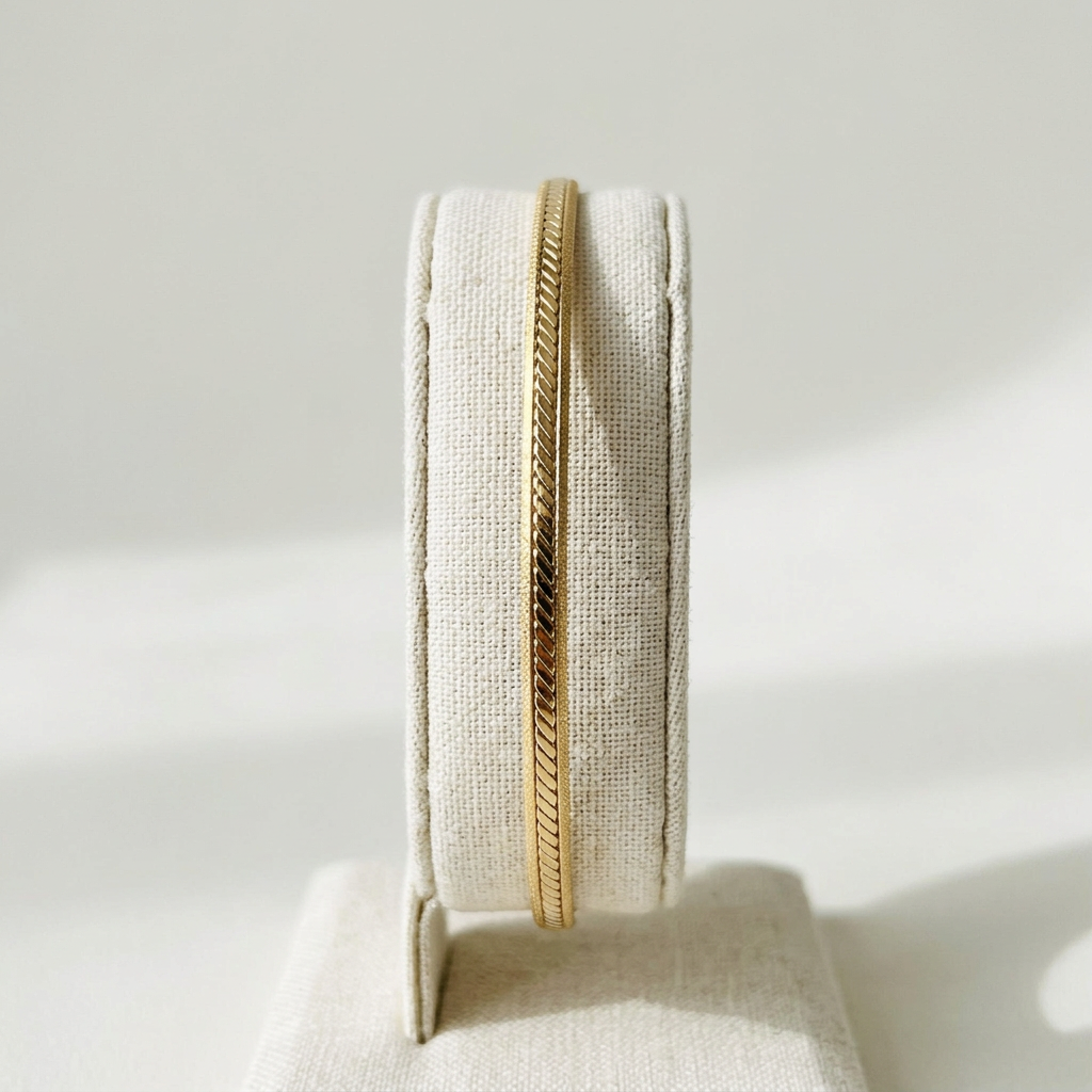 Petit bracelet jonc doré présenté sur un portant en lin ivoire