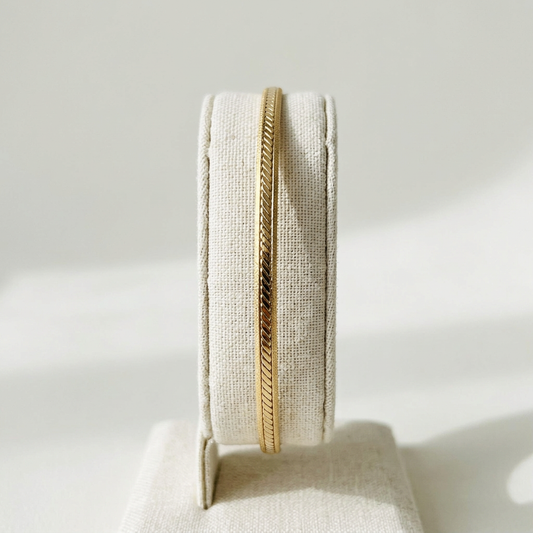 Petit bracelet jonc doré présenté sur un portant en lin ivoire